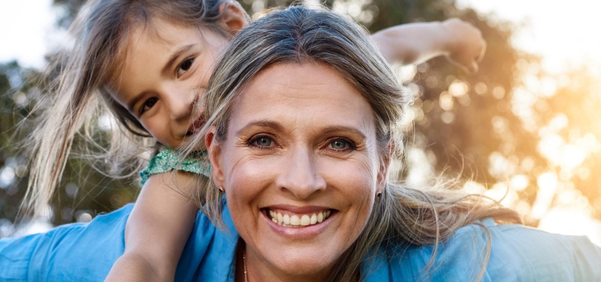 Happy, portrait or mother and daughter with piggyback, love or hug in park for fun, adventure or journey outdoor at sunset. Family, face and mom carrying girl in a forest with support, trust or games.