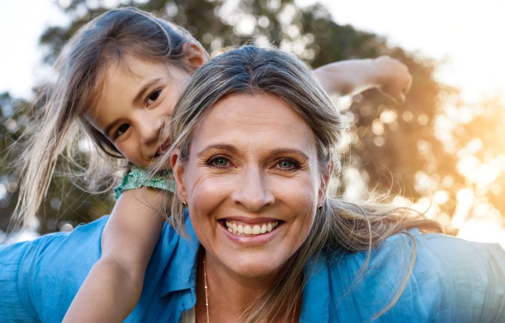 Happy, portrait or mother and daughter with piggyback, love or hug in park for fun, adventure or journey outdoor at sunset. Family, face and mom carrying girl in a forest with support, trust or games.